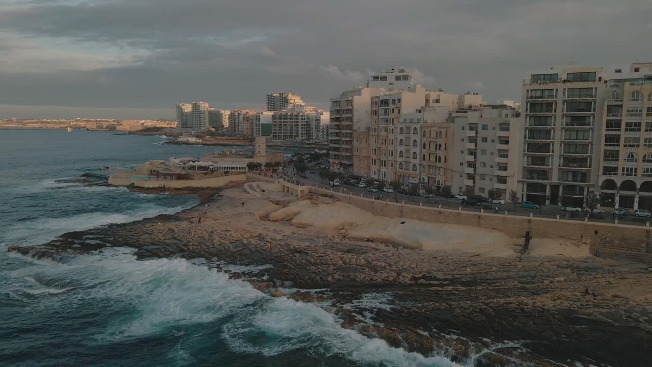 Panoramica aerea della città costiera di Sliema, Malta, mentre le onde si infrangono sulla spiaggia rocciosa