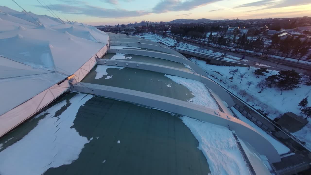 Sweeping FPV drone flight around Olympic Stadium in Montreal, capturing snow and sunset glow