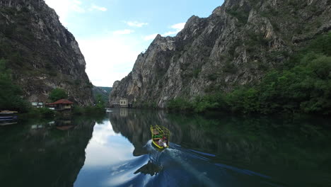 Toma-Aérea-De-Un-Barco-Navegando-En-El-Río-En-El-Día-Soleado-Con-La-Montaña-A-Ambos-Lados