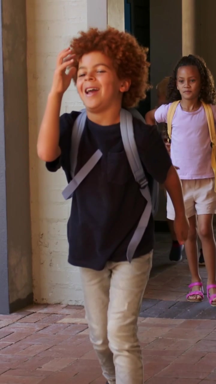 Vertical video: Camera starting, boy in navy t-shirt walking along porch, gray and yellow backpacks