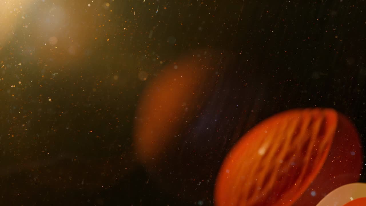 Warm light illuminating airborne dust particles tumbling in dark room, with orange-red lens flare