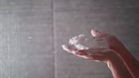 woman blows out foam from hands in shower unit closeup. lady has fun with soap froth while taking bath in home washroom. play with cosmetic product