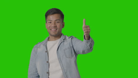 studio shot of casually dressed young man giving thumbs up gesture against green screen