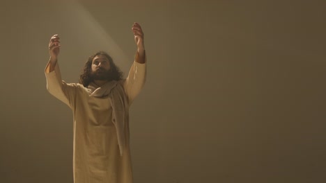 retrato de estudio de tres cuartos de longitud de hombre vestido con túnicas y sandalias con cabello largo y barba que representa la figura de jesucristo orando 1