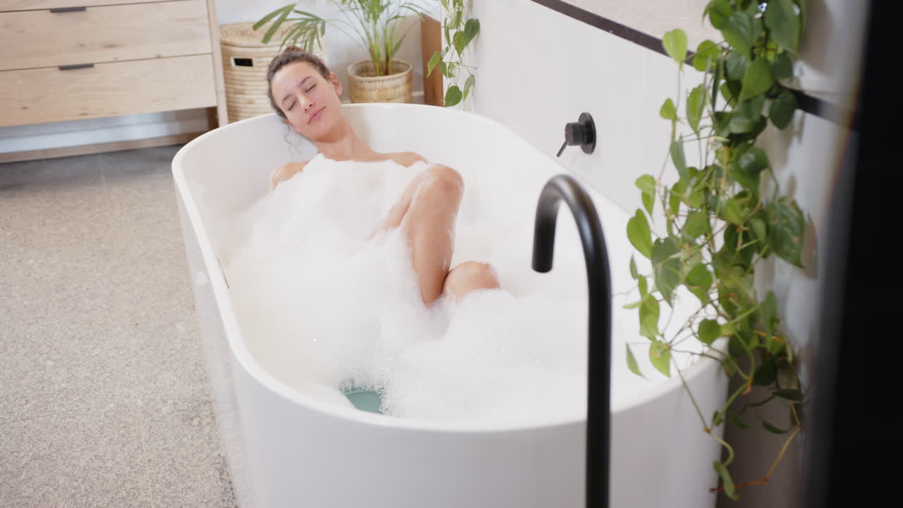 Relaxing in bathtub, woman enjoying bubble bath in modern bathroom home
