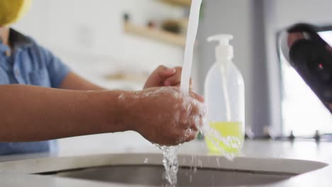 section médiane d'un garçon caucasien debout à l'évier de la cuisine se laver les mains sous le robinet en cours d'exécution