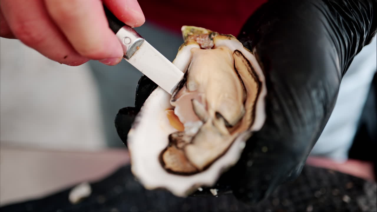 Close up of a waiter cutting a raw oyster at a restaurant