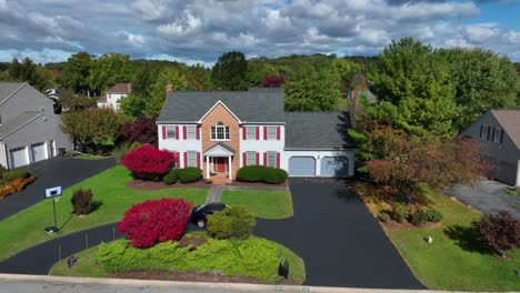 colonial house with red shutters, green lawn, autumn trees, and overcast sky