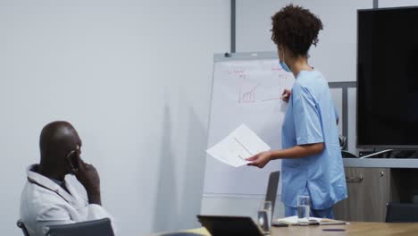 Mixed-race-female-doctor-in-face-mask-giving-presentation-to-african-american-male-doctor-in-office