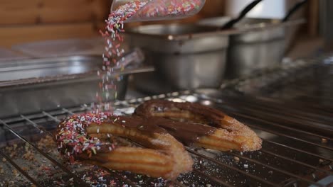 Mit-Frischer-Schokolade-überzogene-Churros-Mit-Mehrfarbigen-Streuseln,-Die-Darüber-Geträufelt-Werden