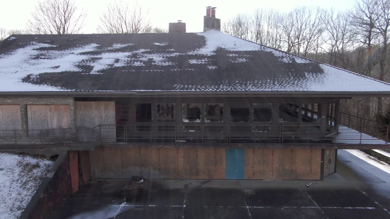 Aerial Drone Footage Dollying Back From a Broken Window to Reveal an Abandoned Lodge.  Boarded Windows, Vandalization, Winter.