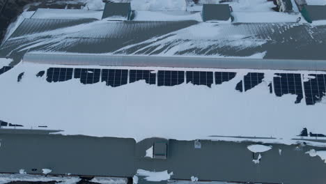 Aerial-dolly-of-snow-covered-solar-panels-on-warehouse-rooftop
