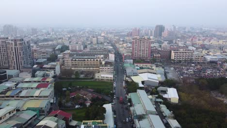 A-bustling-cityscape-with-dense-buildings-and-a-main-road-at-dusk,-soft-light,-aerial-view