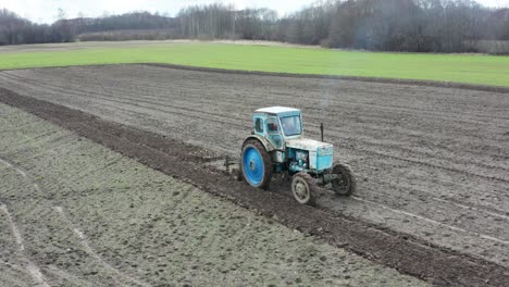 granjero conduce un viejo tractor oxidado en tierras de cultivo, emite gases de escape azules en el aire