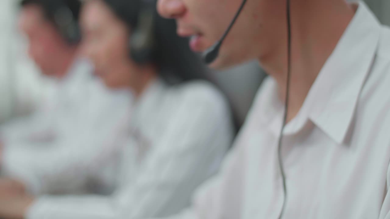 Close Up Of An Asian Man Call Center Agent Wearing Headset Typing On Computer While Speaking To Customer On The Call During Woking With His Colleagues At The Office