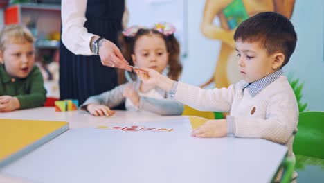little pupils are studying at elementary school. teacher helps children to put picture cards into the necessary place on the table during the lesson.
