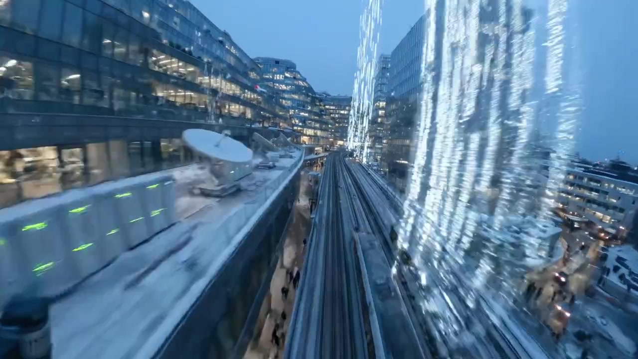 Aerial View of Urban Landscape at Dusk, Featuring Snow-Covered Streets, Glimmering Building Lights, and a Transit Train Moving Through the Cityscape