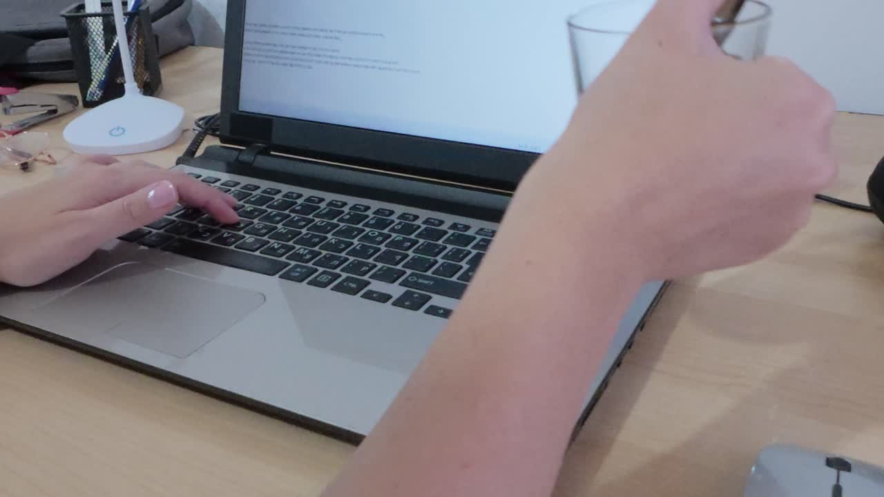 Person working remotely, hands typing on laptop displaying Hebrew text.