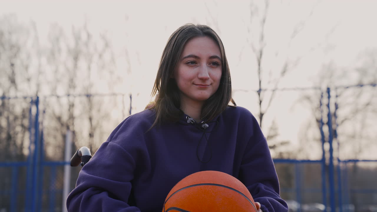 mujer discapacitada feliz en silla de ruedas mirando a la cámara mientras sostiene una pelota de baloncesto en la cancha de baloncesto 2