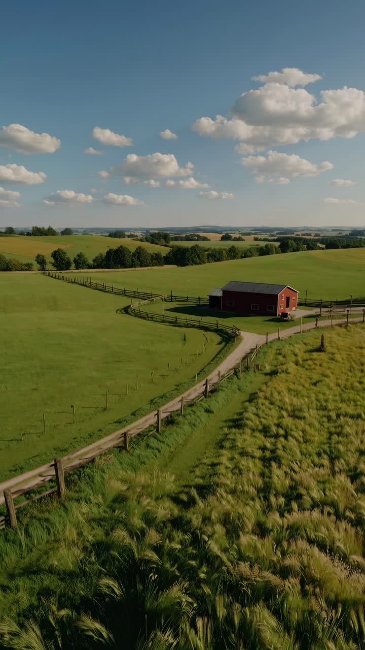 Aerial video captures a serene rural landscape with a winding path, red barn, and lush fields