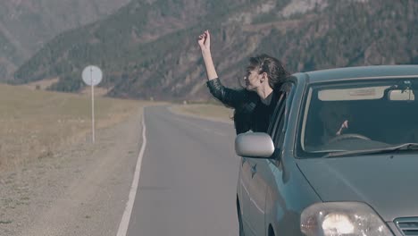 car drives along road with pretty girl leaning out of window