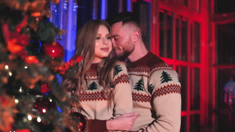 young family kissing near christmas tree. beautiful girl and her boyfriend in knitted christmas sweaters have a romantic evening in new year.