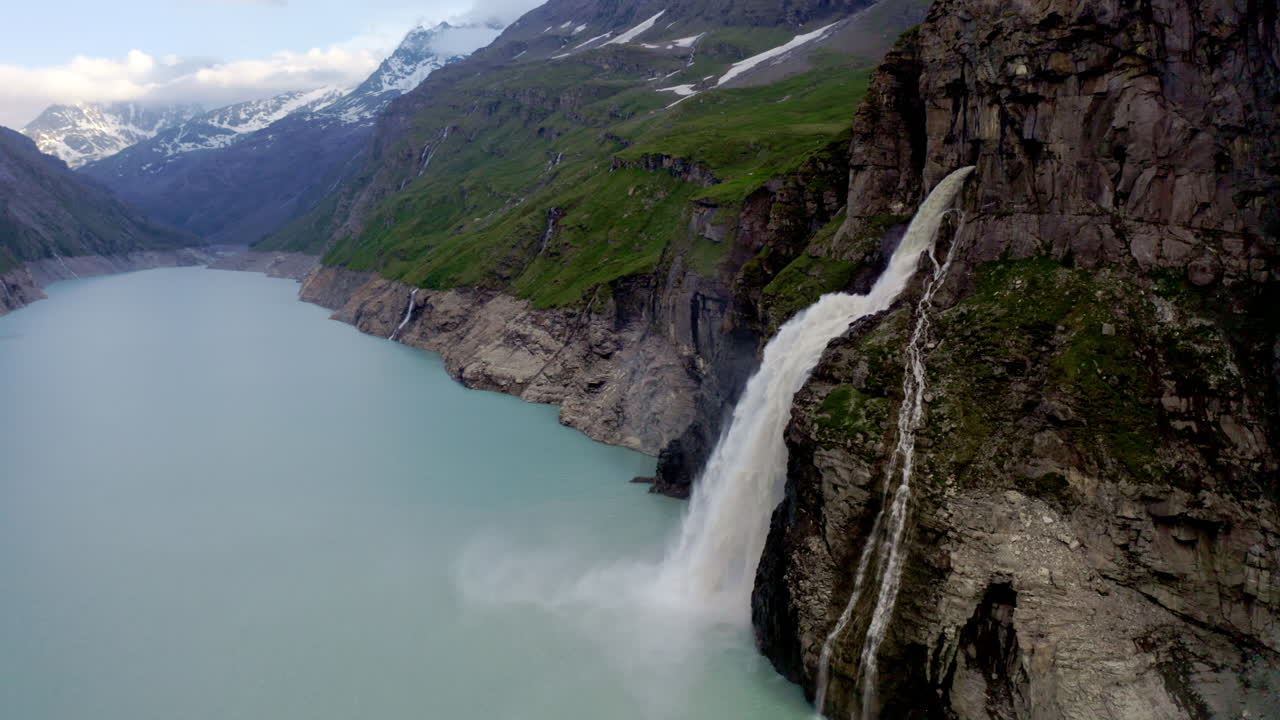 Stunning FPV and drone shots soaring through the Swiss Alps, capturing the Mauvoisin Dam and its majestic waterfall on a clear, sunny summer day.