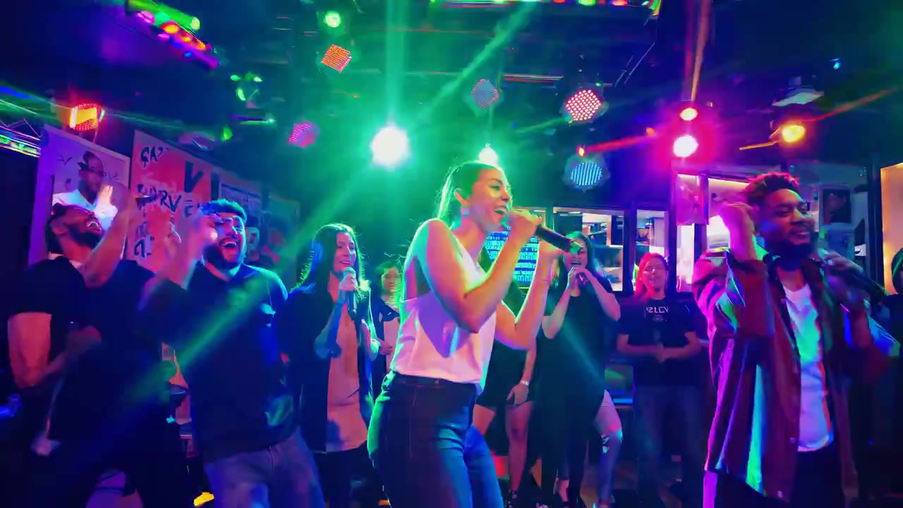 Grupo diverso de amigos cantando karaokê no palco com luzes coloridas