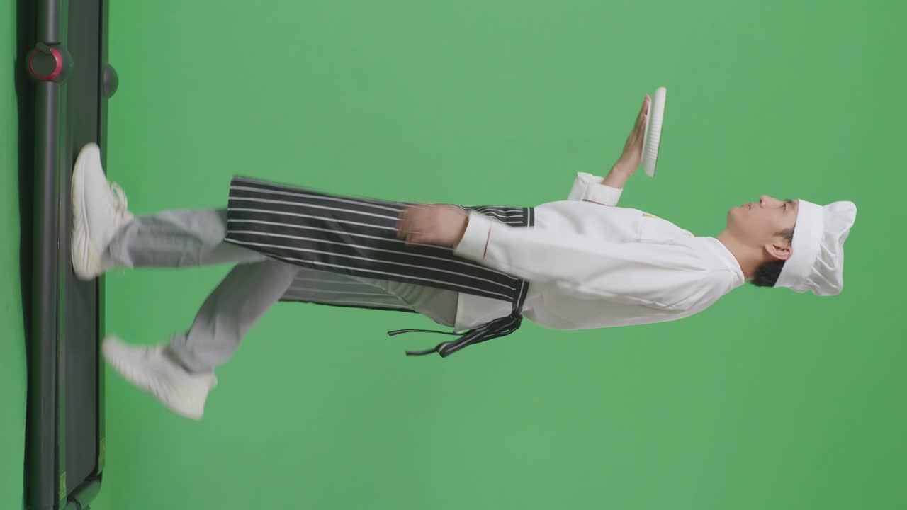 으로 보이는 아시아 남성 셰프가 녹색 스크린 배경 스튜디오에서 트레드밀을 는 동안 접시를 들고 있습니다.