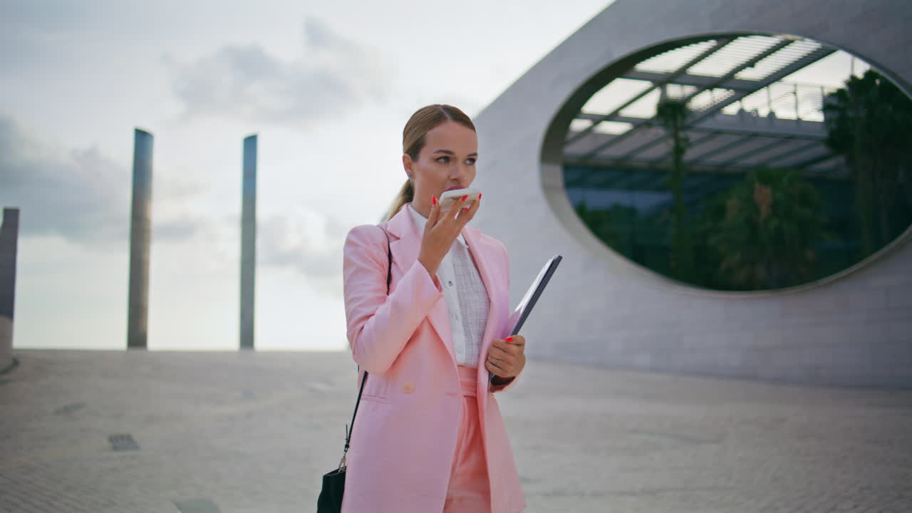 Successful businesswoman recording voice message on smartphone walking street