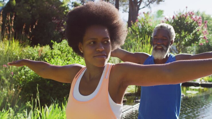 Coppia anziana afroamericana che pratica yoga in piedi in un giardino soleggiato
