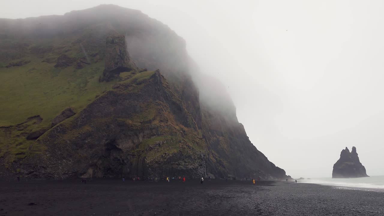 gente caminando por la mística playa de reynisfjara cerca de vik en islandia - ángulo ancho