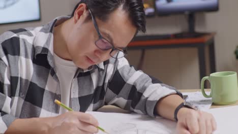 close up of asian male smiling and showing thumbs up gesture to the camera while working on a car design sketch on table in the studio