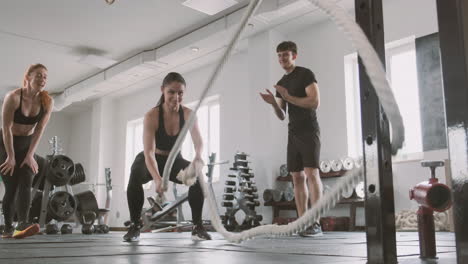 an athletic woman works with battling ropes while gym buddies support her