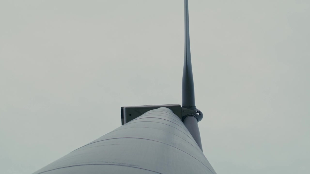 rotating camera looks up at windmill turning in the wind generating clean energy in a field against a partly cloudy sky in smooth, cinematic style and motion.