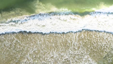 beautiful drone cinematic top view approaching the waves of a brazilian beach with emerald clear water at sunrise