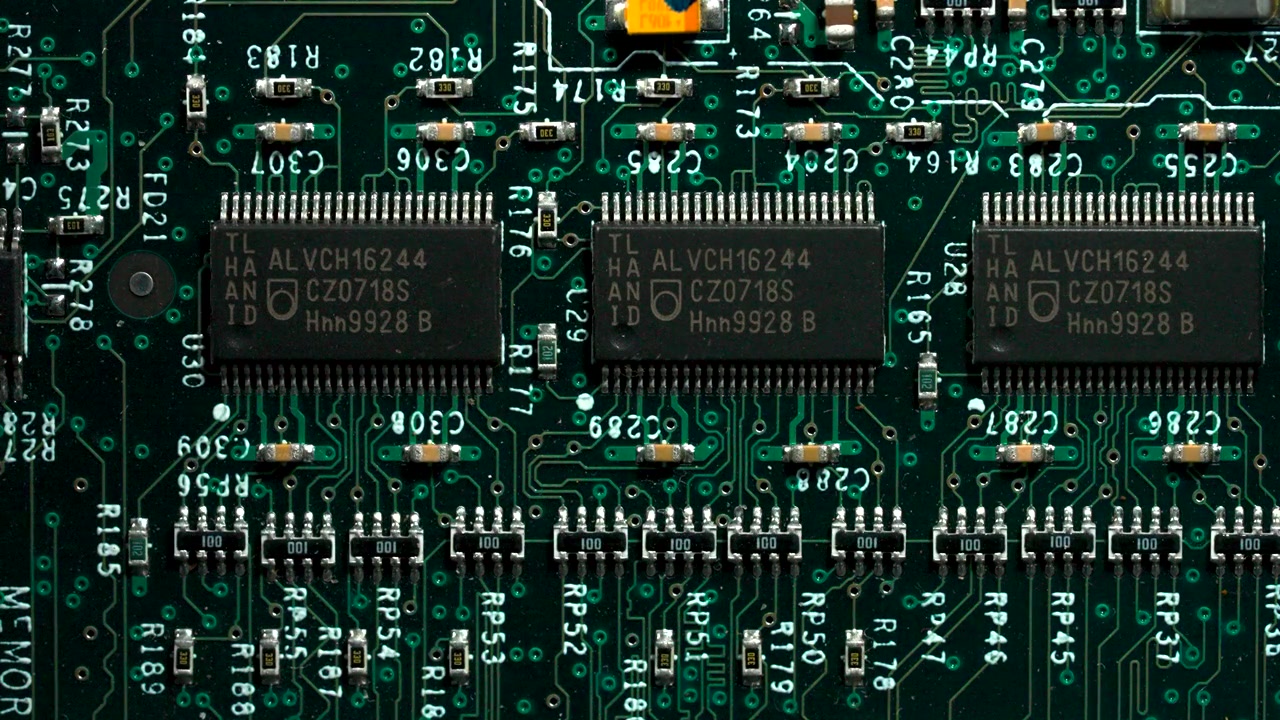High angle detailed shot of a green computer motherboard showing transistors and integrated circuits.