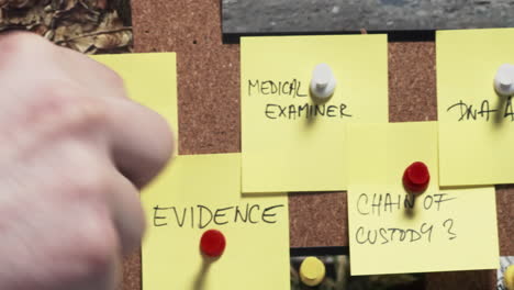 detective's hand wraps red string around pins holding notes on criminal progress on case