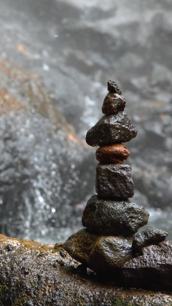 Una pila verticale di rocce in equilibrio su un masso bagnato vicino a una cascata impetuosa