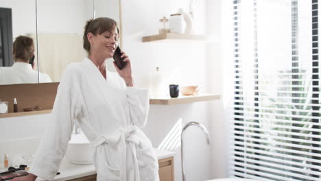 caucasian woman in a white robe talks on the phone, smiling