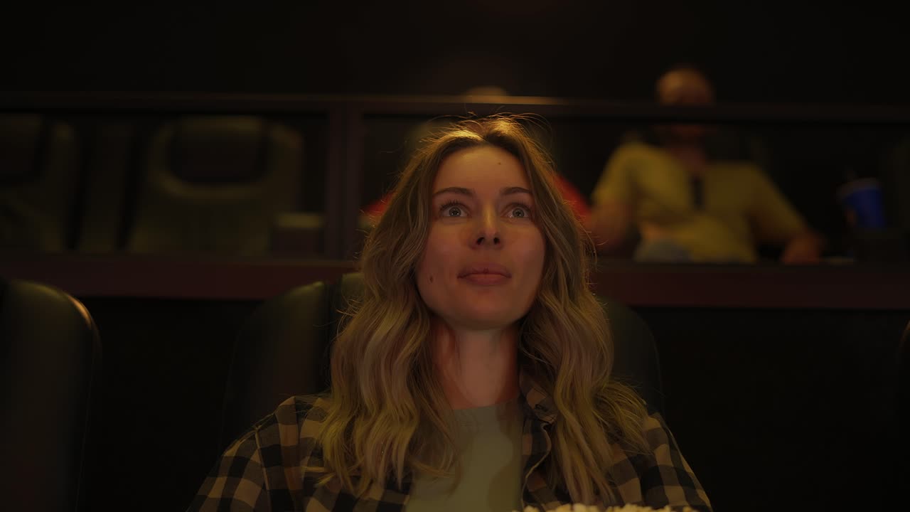 mujer emocionada sentada en un sillón viendo una película en el cine, tomando palomitas de maíz