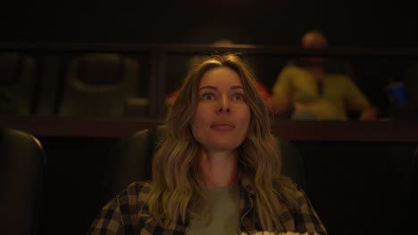 excited woman sitting in armchair watching a movie at the cinema, taking popcorn