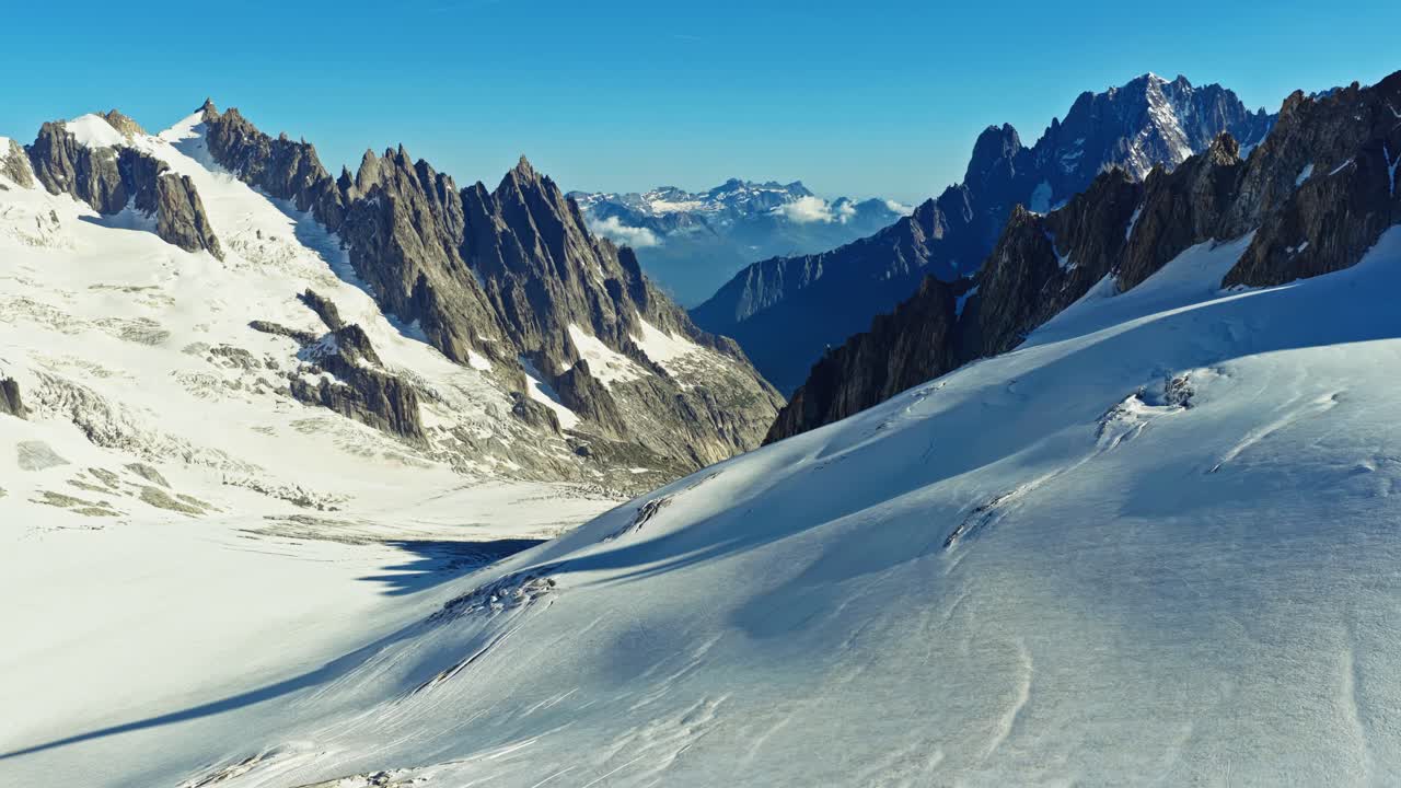 Cinematic aerial view of the French Alps near Chamonix, showing the majestic snow capped peaks and deep valleys of the Mont Blanc massif on a sunny day