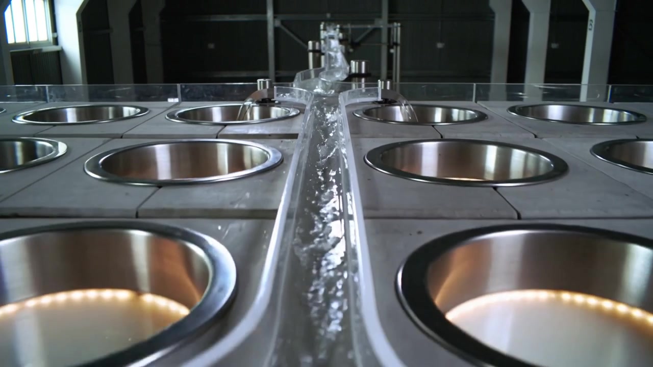 Flowing clear S-shaped channel receiving inflow at top, guiding water into steel basins in workshop