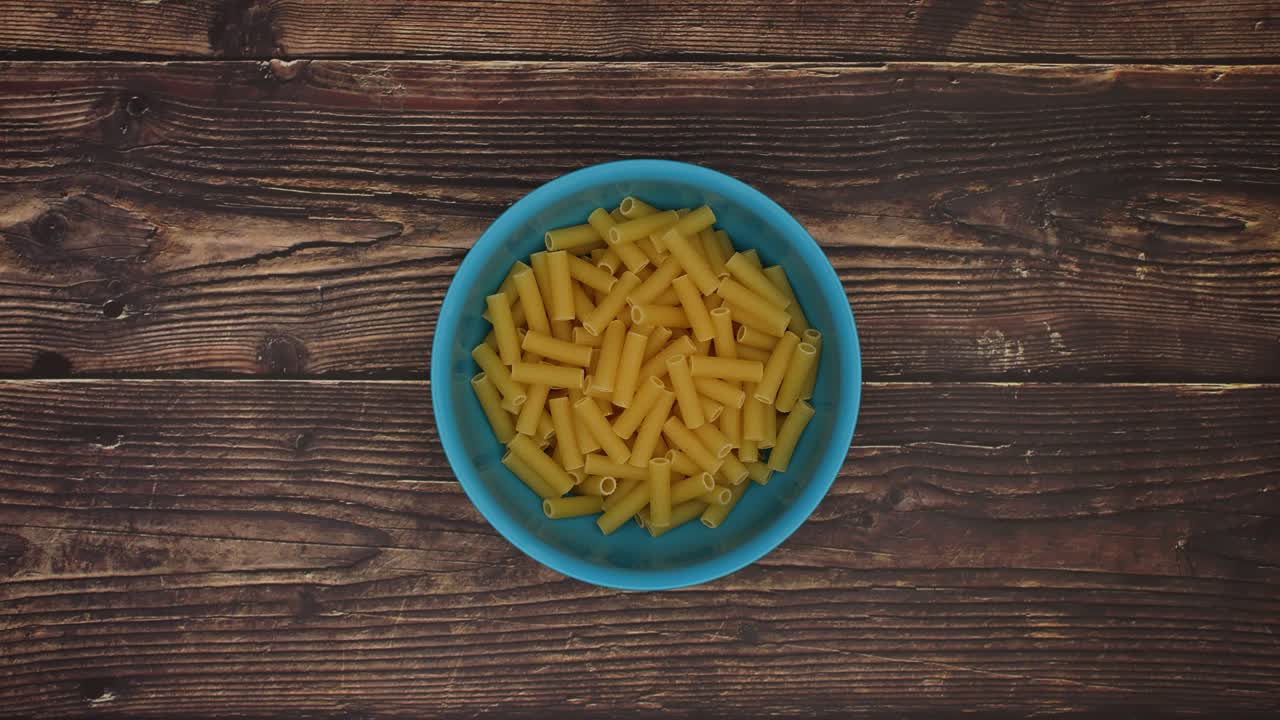 tubetti llenando el cuenco azul sobre un fondo de madera - movimiento de parada
