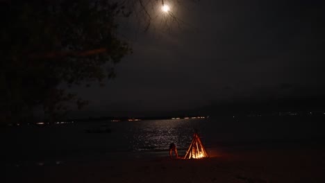 hoguera en la playa bajo la luna llena reflejada en el mar, destino de viaje tropical de komodo en indonesia