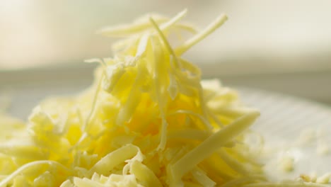 small pile of freshly grated british mature cheddar cheese on plate in natural light. healthy dairy based food. rich in protein and calcium