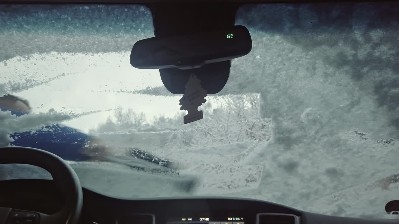 una vista del parabrisas nevado de un automóvil, desde el cual un hombre está limpiando la nieve