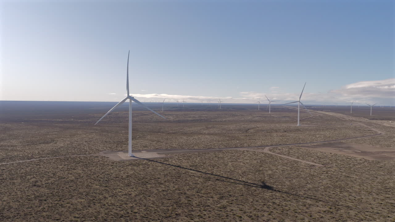 Drone view of tall wind turbines turning slowly, producing clean renewable energy over a wide open landscape