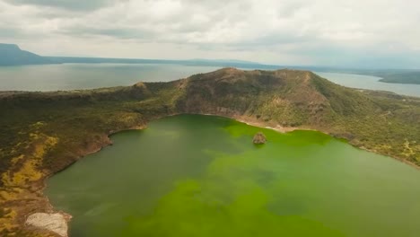 Aerial drone footage flying over Taal lake or Bombon lake during a beautiful day with some clouds and sun shining on the lake. The water is green and vibrant and nature lush green landscape around it.
